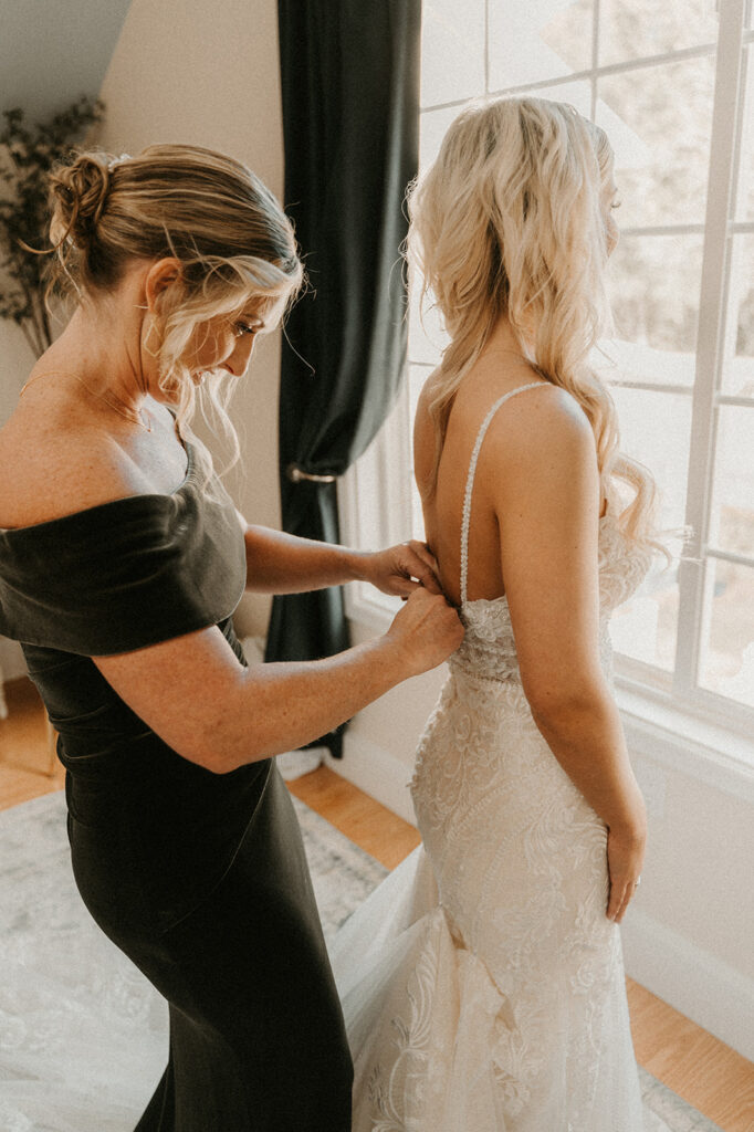 mother of the bride helping her with the dress before her boho wedding 