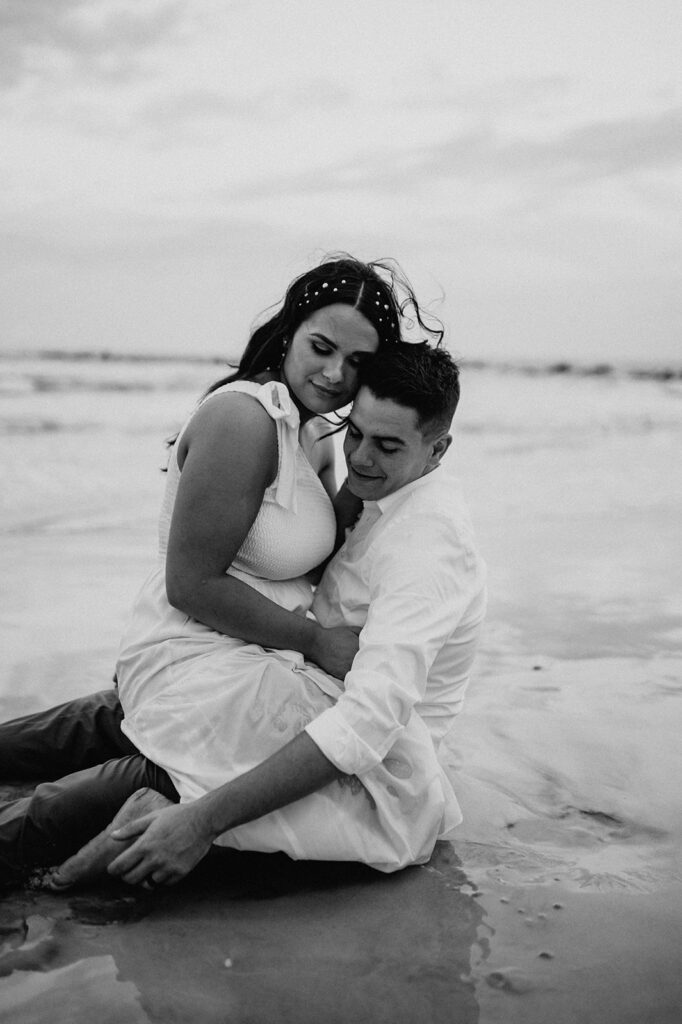 couple sitting at the beach during their moody engagement session