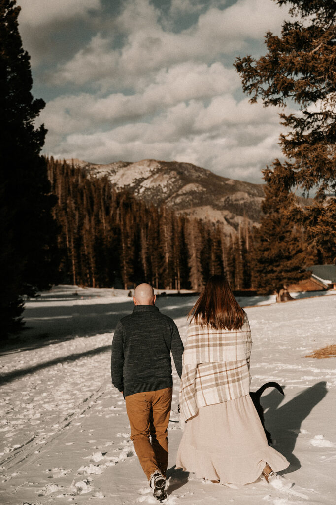 cute couple holding hands walking during their snowy & adventurous engagement session